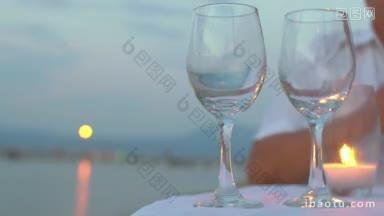 在户外餐厅里，一个男人拿着蜡烛站在桌子上，把白葡萄酒倒进两个杯子里
